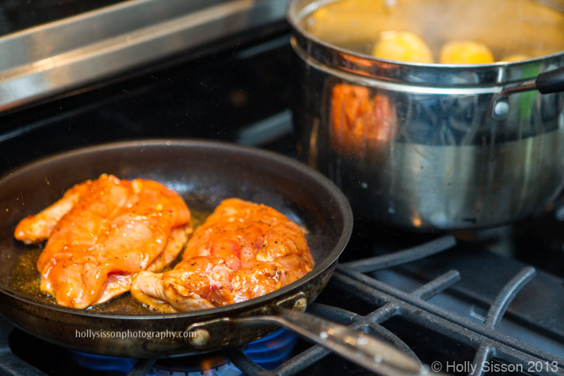Chicken in pan on stove top beside corn cobs in pot
